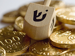 A dreidel sits on top of a pile of chocolate gelt, a treat popular in Jewish holiday tradition.