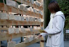 A visitor hangs a wooden plaque with her wishes written on it at Meiji Shrine in Tokyo. More than three million people visit the Meiji Shrine during the first three days of the New Year, to pray for their health, economic fortune and wishes to come true